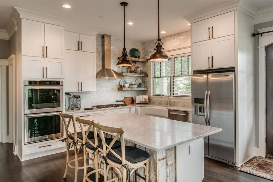 - Modern kitchen with white cabinets stainless appliances and island   - Wood textures and pendant lighting create a warm inviting space   - Perfect cooking setup for groups who love home style meals
