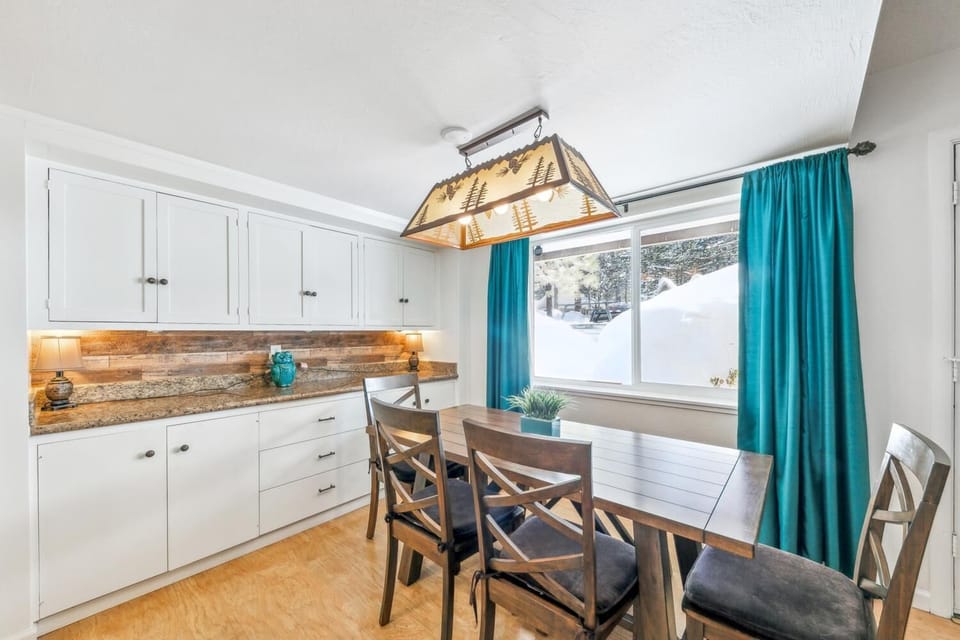 Your bright kitchen-dining space features rustic wood accents, modern appliances, and turquoise curtains framing snowy mountain views.