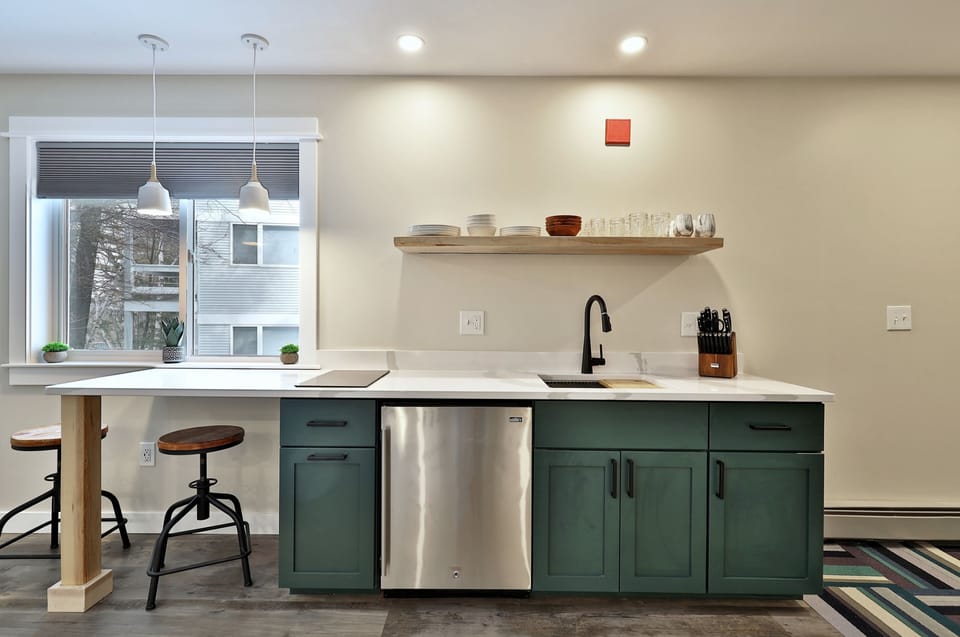 Kitchenette equipped with bar stools mini fridge and two burner stovetop.