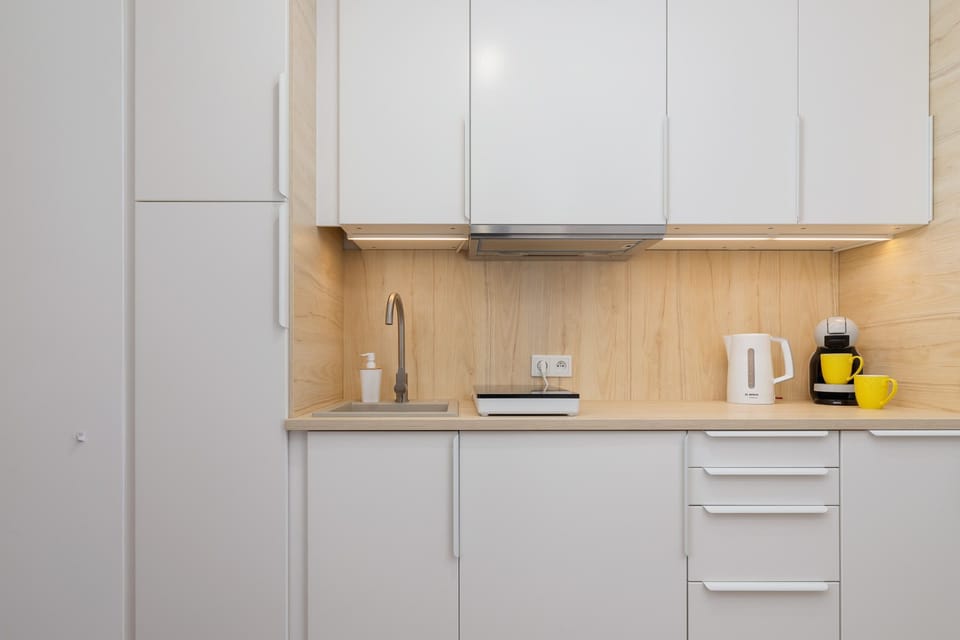 A sleek kitchenette with white cabinets, wooden accents, and compact appliances.
