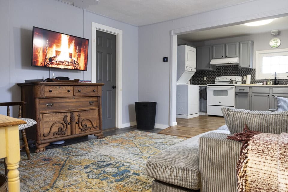 Farmhouse Living Room – The farmhouse living room features a comfortable couch, TV, and curated artwork, along with a side table for added convenience. The open layout provides easy access to the kitchen and bedrooms, creating a welcoming and functional g