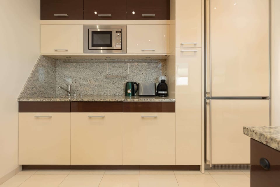 A kitchenette with light cabinets, granite countertops, and modern appliances.
