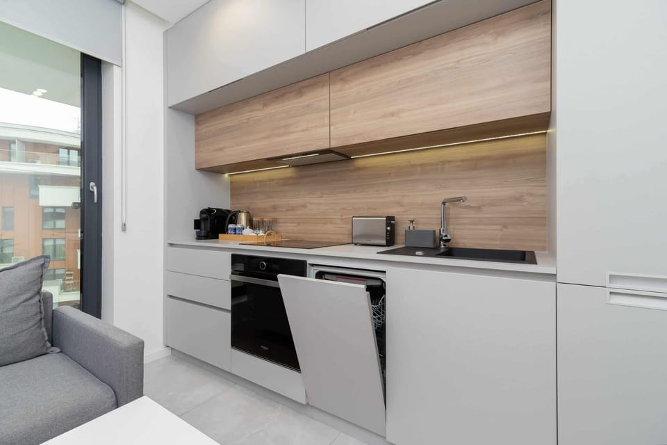 A modern kitchenette with sleek cabinetry and a window overlooking the balcony.
