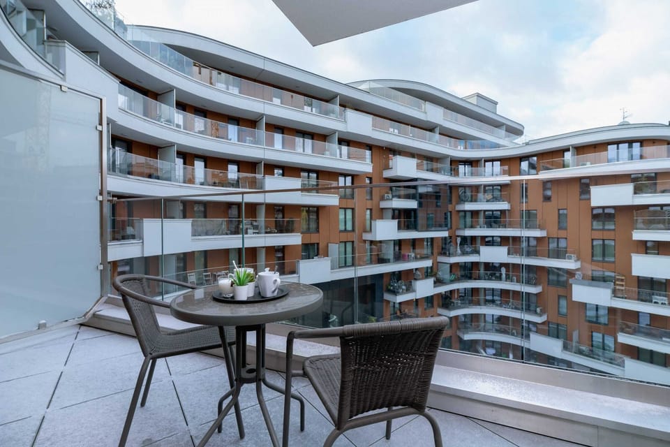 A balcony with a small table and chairs, overlooking a contemporary apartment complex.
