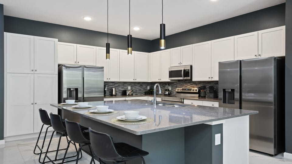 Modern chef’s kitchen with dual fridges, sleek island seating, and bold design.
