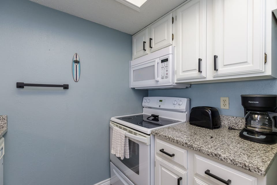 Your fully equipped kitchen features granite countertops, white appliances, and soothing blue walls. Everything you need for home-cooked meals during your stay.