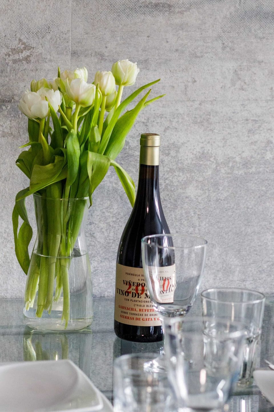 A dining table with a vase of flowers and wine, set for a perfect evening.

