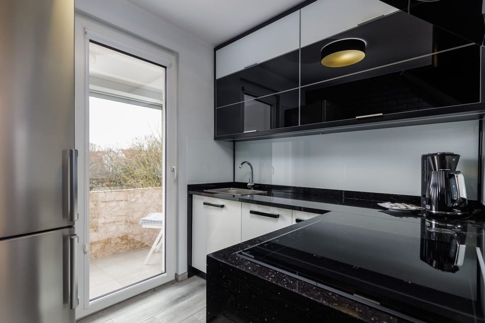 A black-themed kitchen with glossy cabinets, sleek appliances, and a large window.
