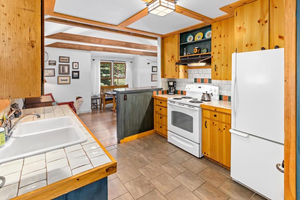 Tile countertops with warm wood cabinetry and white appliances define the kitchen space