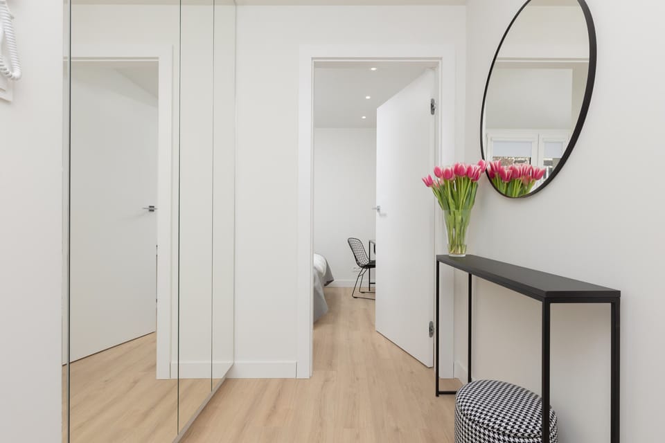 A minimalist hallway with a round mirror and a small table with a floral vase.
