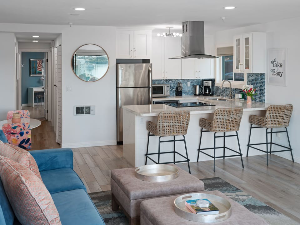 Open plan kitchen within living room space including a comfortable sofa, and coffee table. Kitchen bar with 3 bar stools for dining/ breakfast