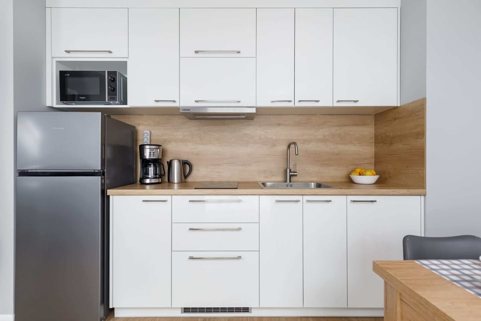 A white kitchen with a wooden countertop, fully equipped with modern appliances.
