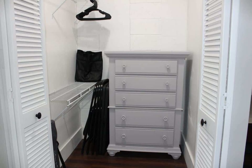 Master bedroom walk in closet with 2 wire shelves, full size dresser, card table & 4 chairs, pack n' play and high chair.