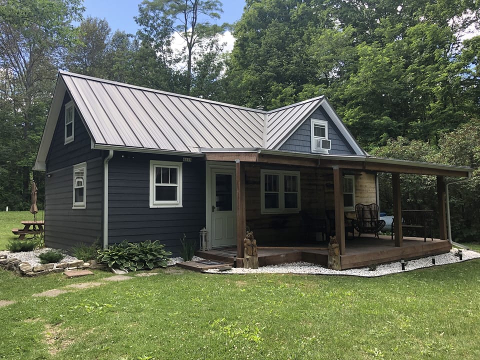 Front of the cottage. Porch has furniture, a ceiling fan, and metal roof.