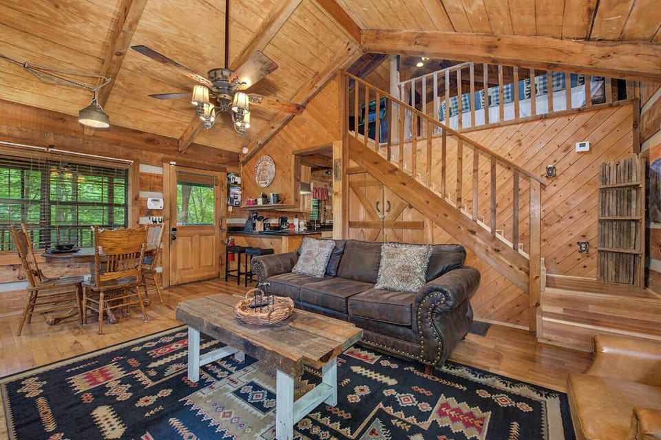 Unwind in your cozy cabin retreat with vaulted wood ceilings, plush seating, and a rustic staircase leading to the loft. Enjoy warm meals at the dining table or relax as natural light pours through the windows.