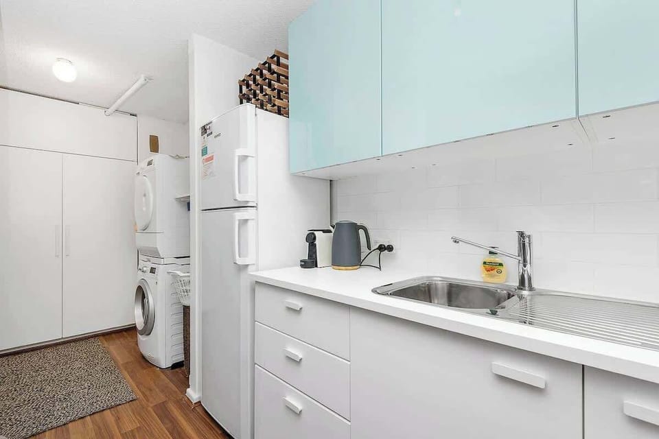 This neat and efficient space combines a functional kitchen with a refrigerator, sink, and ample kitchen cabinets, alongside a convenient laundry area equipped with a washer and dryer.