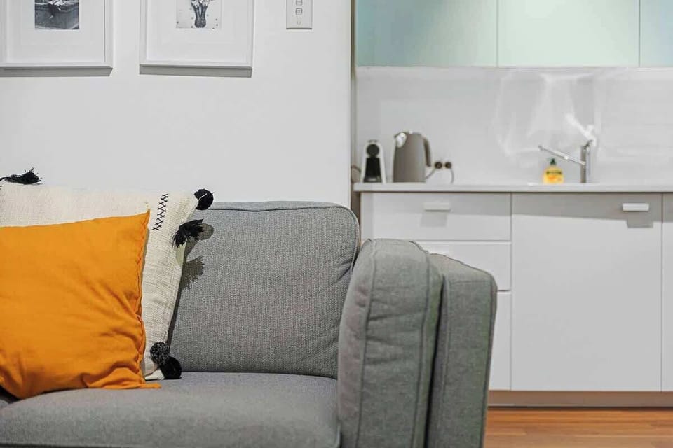 Relax on the comfortable sofa with stylish cushions, offering a partial view into the adjacent kitchen area.