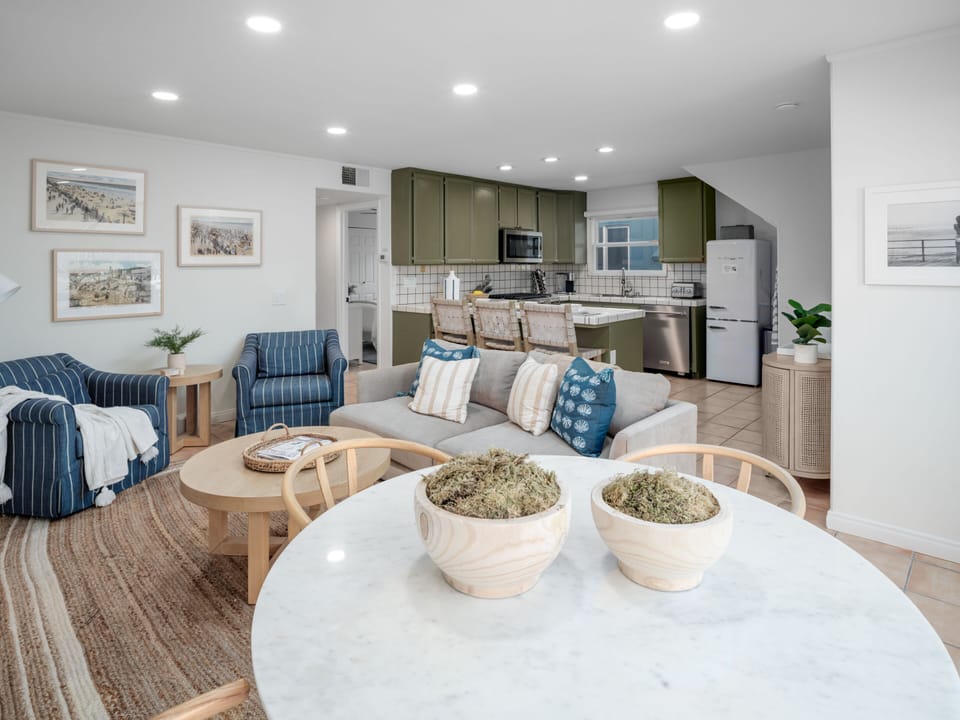 Featuring natural wood, soft blues, creams, greens, and earthy tones, this living space with a dining area seamlessly integrates an open-plan kitchen for perfect interaction among guests.