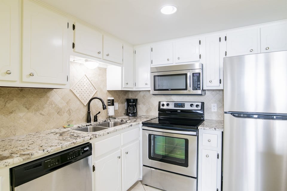 Kitchen With Stainless Steel Appliances, Coffee Maker, Blender, Mixer, Toaster And Plenty Of Pots, Pans And Dishes And Tiled Backsplash