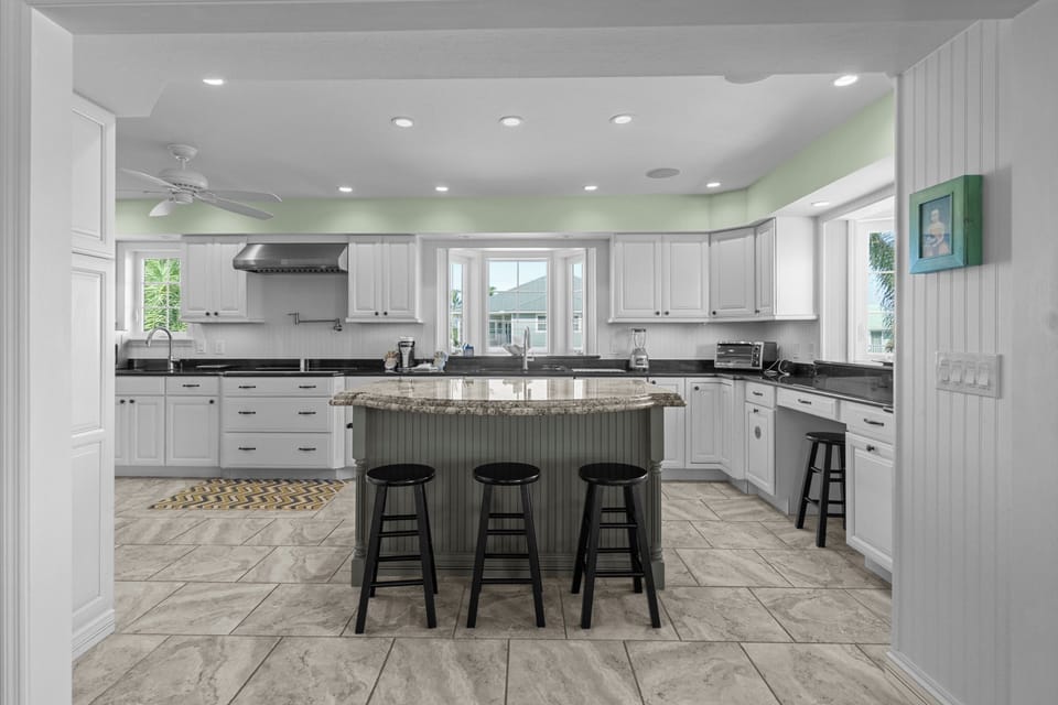 Spacious coastal kitchen featuring a large granite island with seating, stainless steel appliances, and bright white cabinetry—perfect for gathering and entertaining.