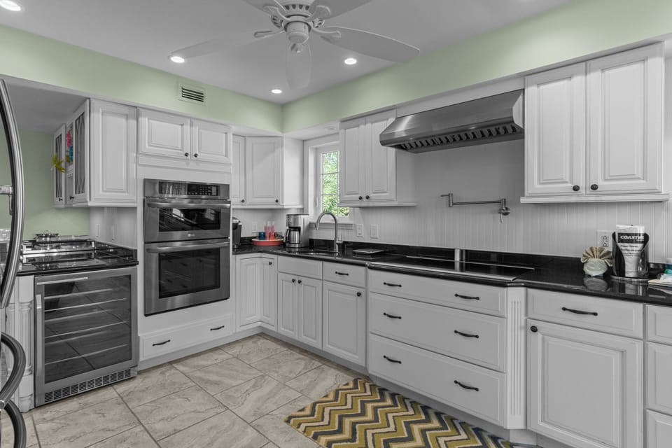 Spacious coastal kitchen featuring a large granite island with seating, stainless steel appliances, and bright white cabinetry—perfect for gathering and entertaining.