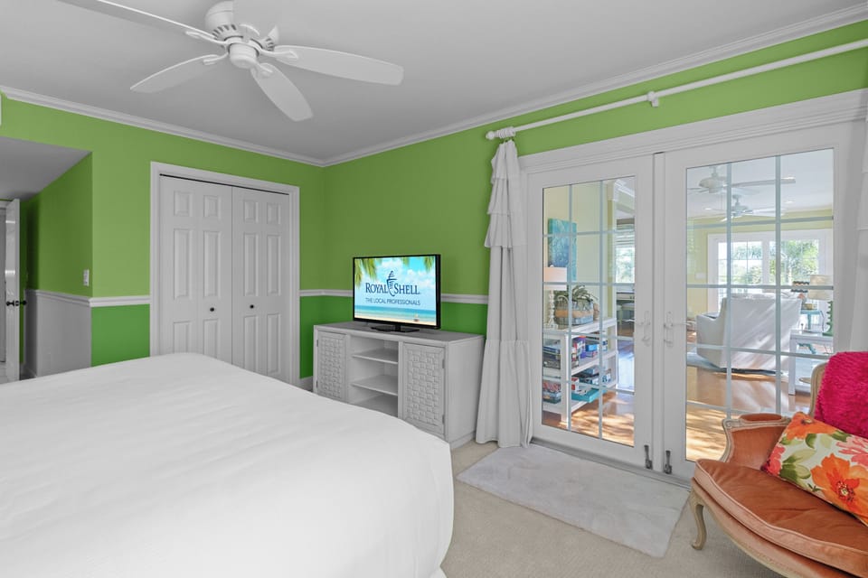 Vibrant guest bedroom featuring bold green walls, crisp white bedding, and French doors leading to the sunroom for added light and space