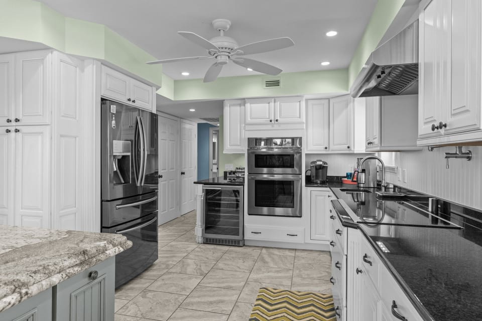 Spacious coastal kitchen featuring a large granite island with seating, stainless steel appliances, and bright white cabinetry—perfect for gathering and entertaining.