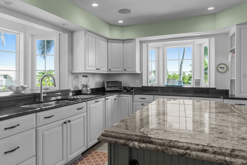 Spacious coastal kitchen featuring a large granite island with seating, stainless steel appliances, and bright white cabinetry—perfect for gathering and entertaining.