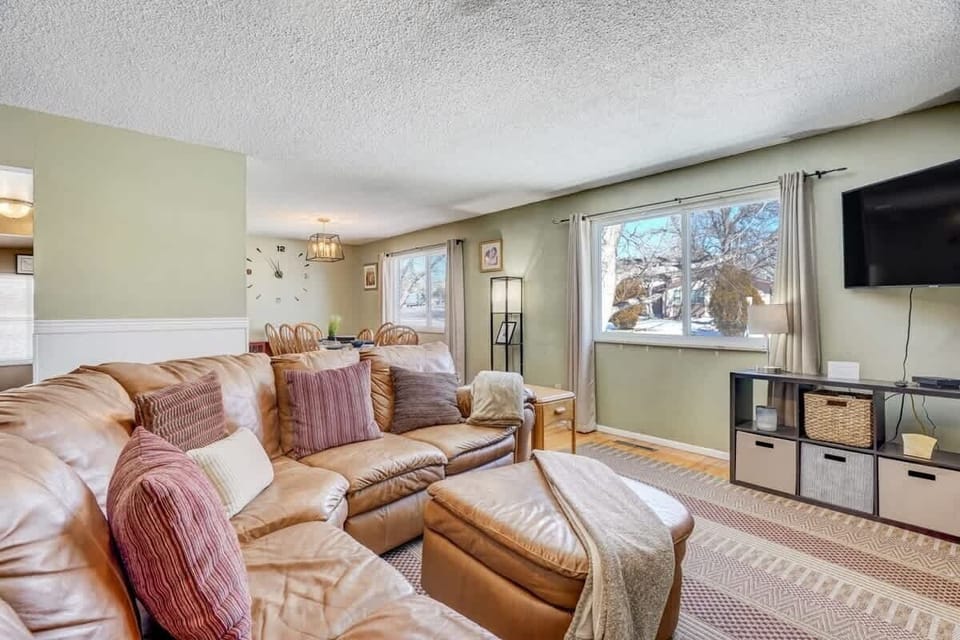 Sink into the roomy leather sectional with patterned pillows, facing the wall-mounted TV. Big windows and airy curtains make it easy to linger over coffee, then stretch out on the rug for a slow, cozy evening in. Woven baskets keep things tidy today.