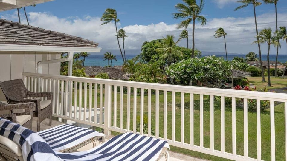 Relax on a private balcony with cushioned loungers, overlooking lush palm trees and sparkling ocean views.