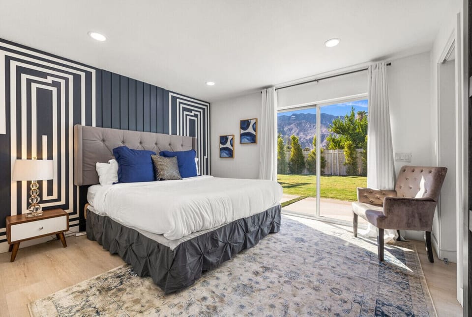 Bright bedroom w/ statement headboard, cozy seating, & sliding doors opening to fresh air.