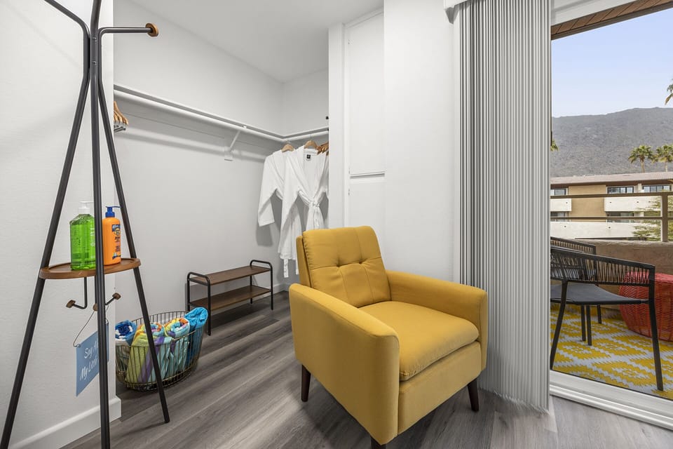 - Cozy reading nook with yellow chair and open closet storage   - Robes and pool towels ready for a day of comfort or sun   - Bright natural light and balcony access enhance vacation vibes