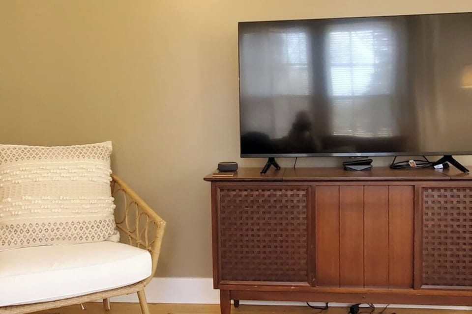 Cozy living area with a flat-screen TV, mid-century console, and a cushioned rattan chair—perfect for relaxing in comfort and style.