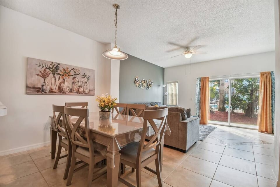Bright and airy, this dining area features a spacious wooden table, perfect for family meals or games. Large windows adorned with warm curtains invite natural light, offering a seamless connection to the outdoor greenery.