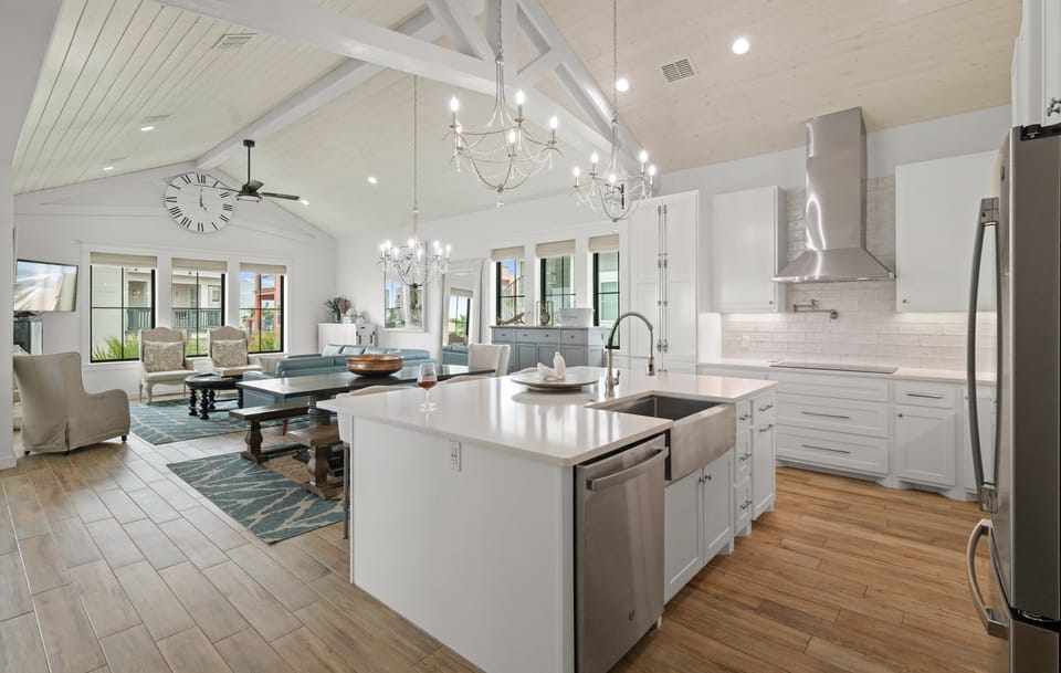 Open Floor Plan — Kitchen Island with Farmhouse Sink, Chandeliers, Exposed Beams, Blue Sectional & Stainless Range Hood