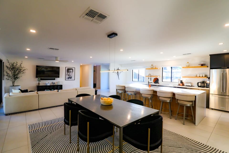 Open-concept great room with a spacious sectional, abundant natural light, a large HDTV with cable, and seamless flow to the dining area and fully equipped kitchen.
