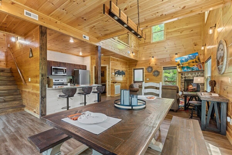 Rustic open-concept living area with vaulted ceilings, a stone fireplace, and a fully equipped kitchen.