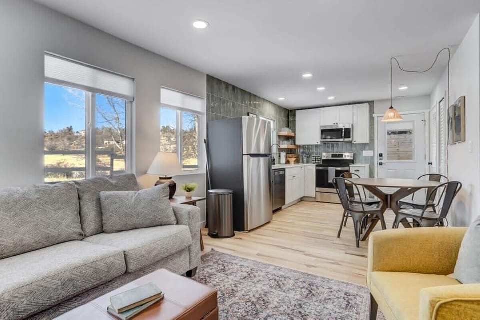 The space is flooded with natural light from the large windows, and the open floor plan with the kitchen creates a spacious feel.