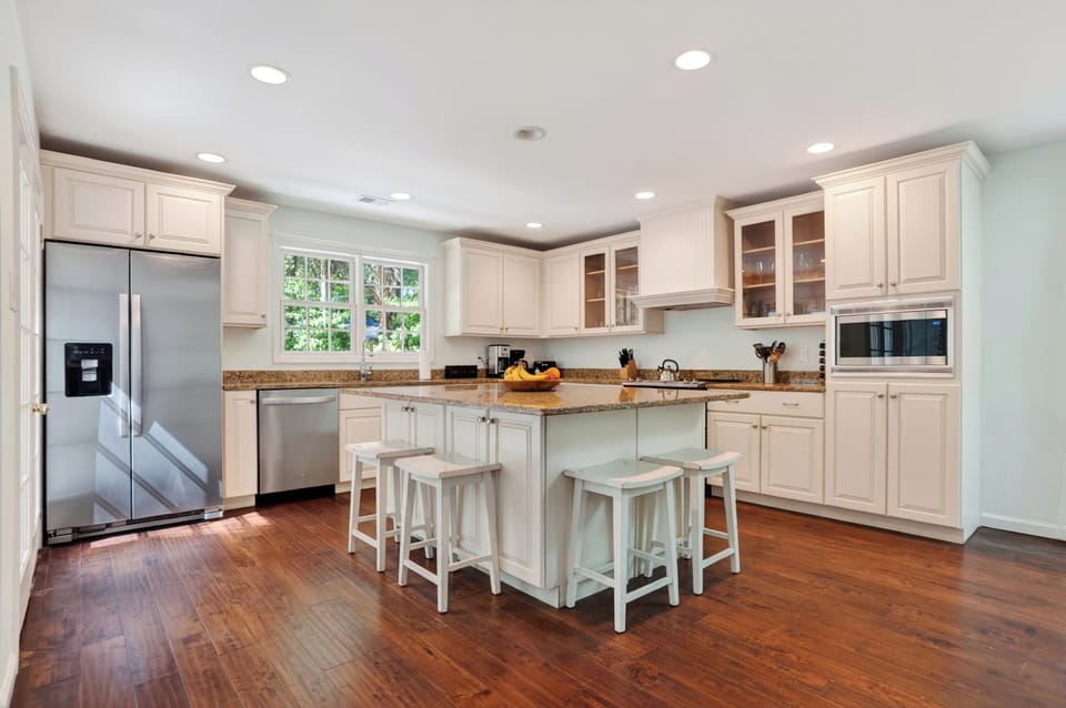 Bright modern kitchen with crisp white cabinetry, granite island seating, and warm natural light pouring in.