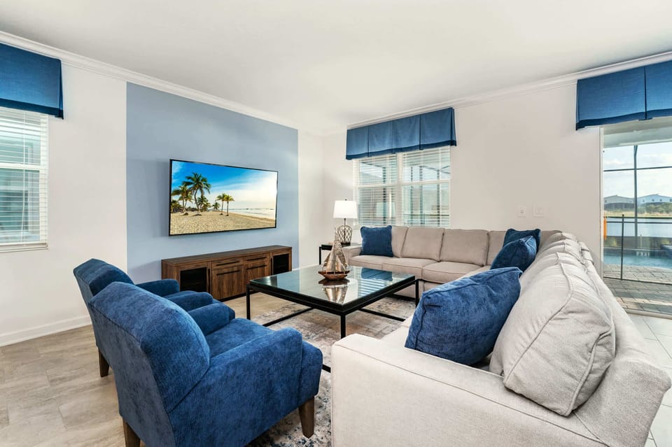 Relax in this spacious living room with plush seating, a large TV, and abundant natural light, perfect for family gatherings.