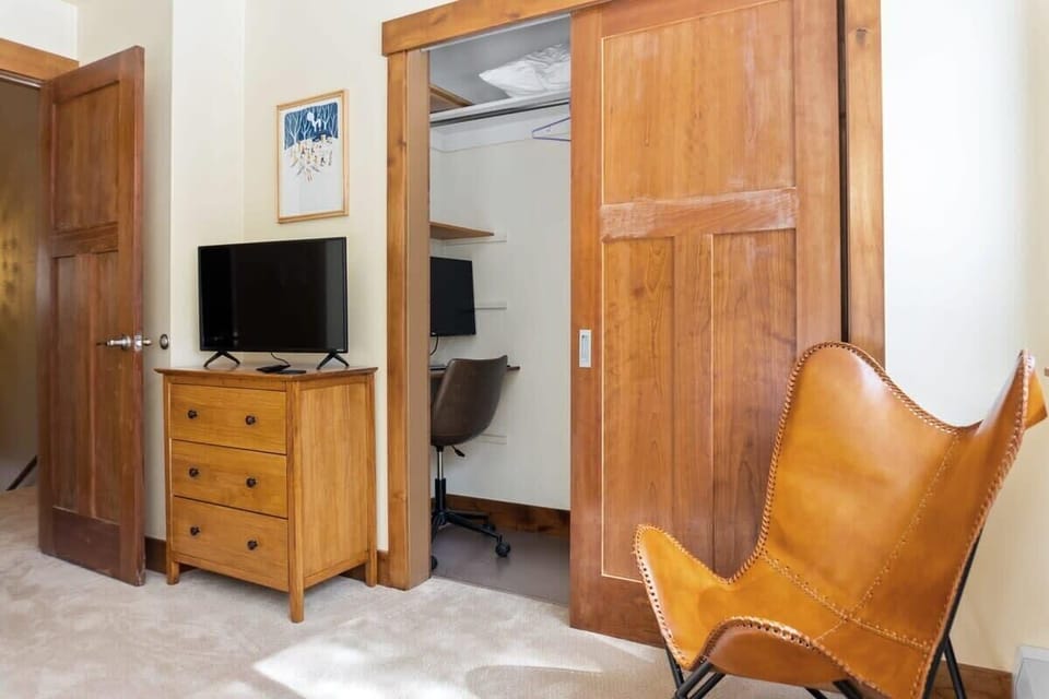 The master bedroom includes a closet with a small desk and a monitor for a private workspace, a reading chair, a dresser, and a 32” TV.