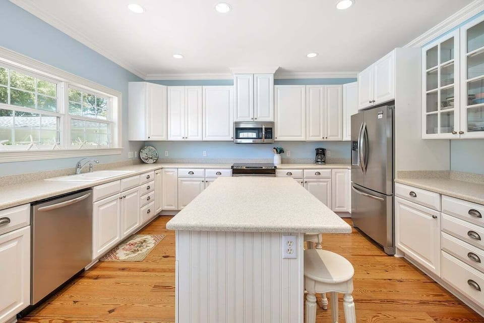 White kitchen with island, stainless appliances, and wood floors