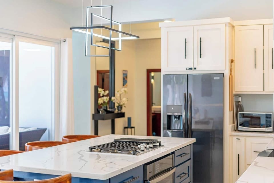Modern kitchen detail with stainless steel fridge, gas cooktop, and hallway view with decorative accents on Ambergris Caye
