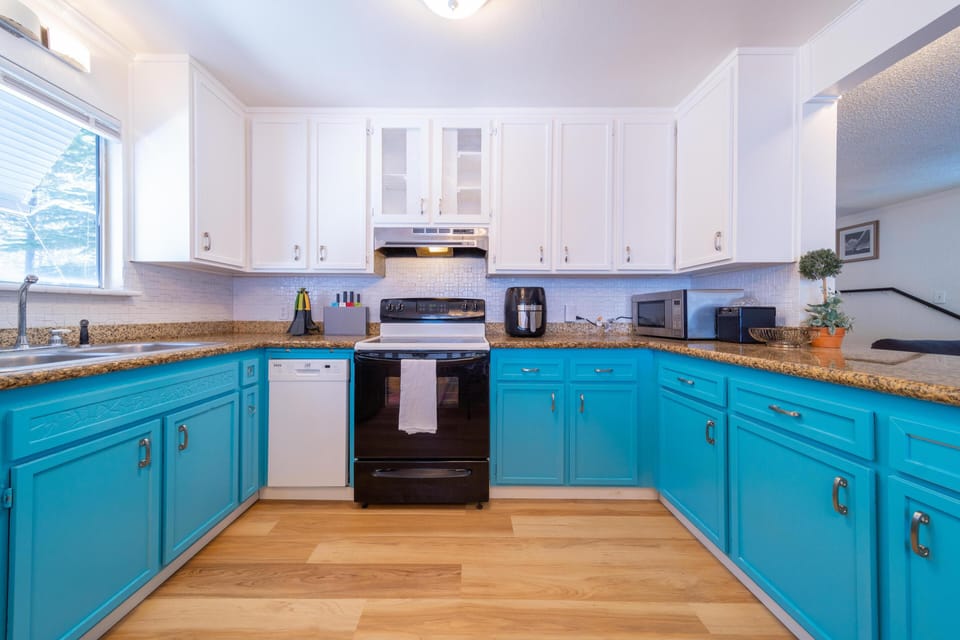 U-shaped kitchen with turquoise lower cabinets, white upper cabinets, granite countertops, and black stove.