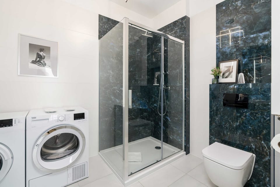 Modern bathroom with toilet, glass shower stall, sink with mirror, washing machine and dryer.