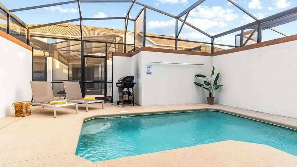 Private screened-in pool area featuring lounge chairs, a BBQ grill, and vibrant greenery. Perfect for relaxing under the sun or enjoying a family BBQ in a serene and secure setting.