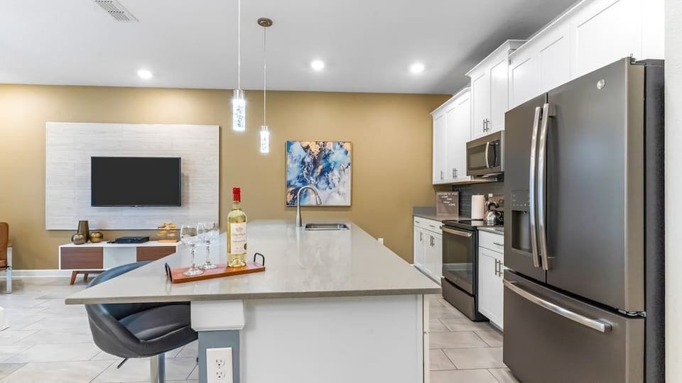 Modern kitchen with sleek stainless steel appliances, a spacious island with seating, and elegant pendant lighting. The open layout flows into a cozy living area, perfect for entertaining or enjoying a relaxing evening at home