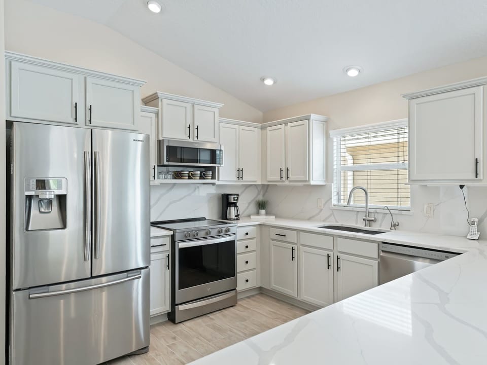 Well-lit kitchen with all stainless steel appliances.