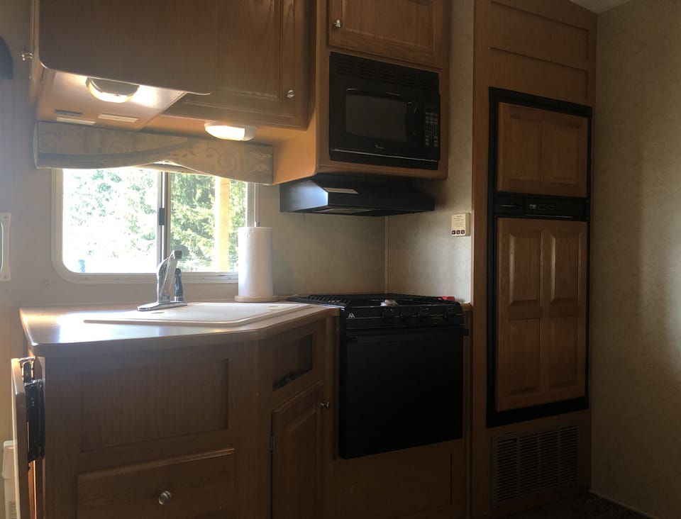Inside RV, kitchenette with fridge, freezer, microwave, gas stove and sink. 