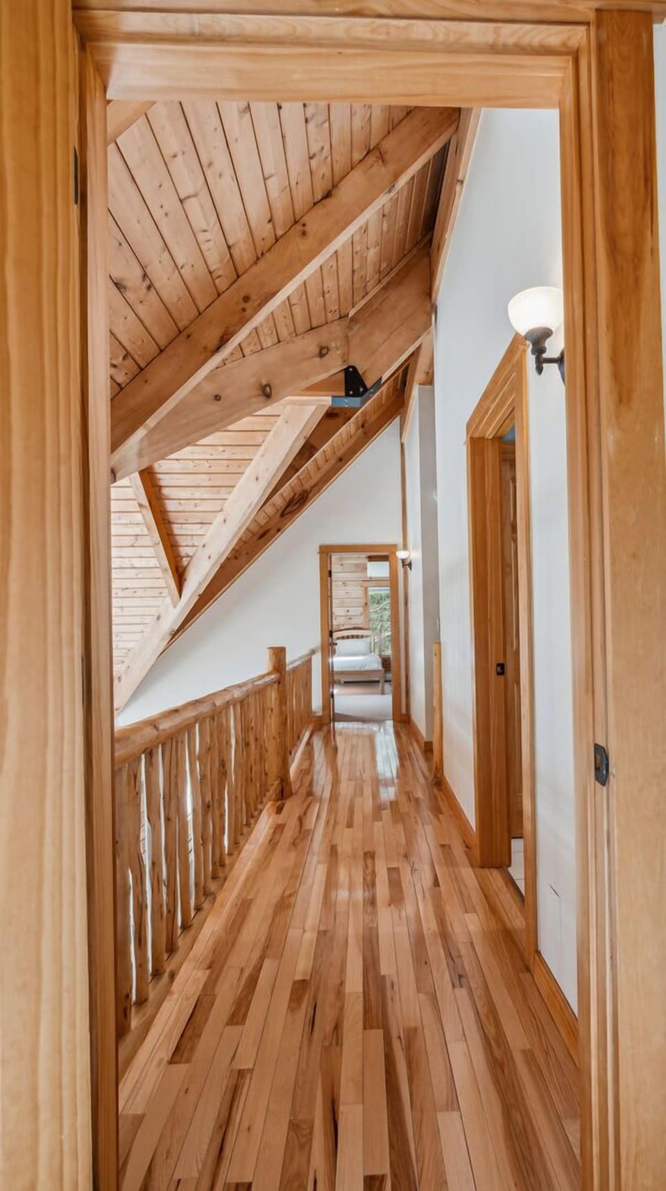 Upper-level hallway with exposed timber
    trusses and log railing overlooking the
    great room below